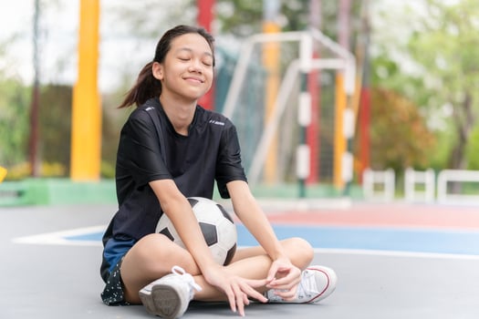 Asian kid girl with a ball sitting on outdoor futsal sports field photo