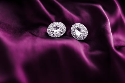 Luxury diamond earrings on dark pink silk fabric, holiday glamour jewelery present photo
