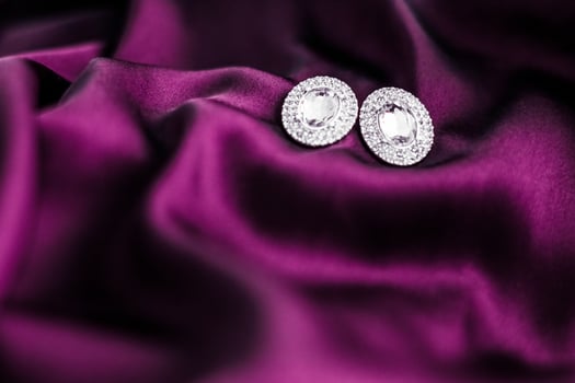 Luxury diamond earrings on dark pink silk fabric, holiday glamour jewelery present photo