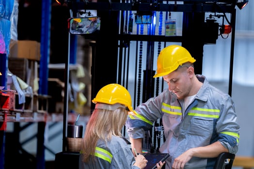 Two male and female factory checkers are discussing work on a warehouse truck. While working in a warehouse for industrial products photo
