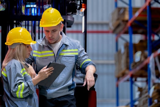 Two male and female factory checkers are discussing work on a warehouse truck. While working in a warehouse for industrial products photo