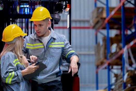 Two male and female factory checkers are discussing work on a warehouse truck. While working in a warehouse for industrial products photo