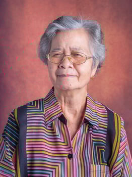 Portrait of a beautiful senior Asian woman wearing glasses with short white hair smiling and looking at the camera while standing with a vintage background. Concept of aged people and healthcare photo