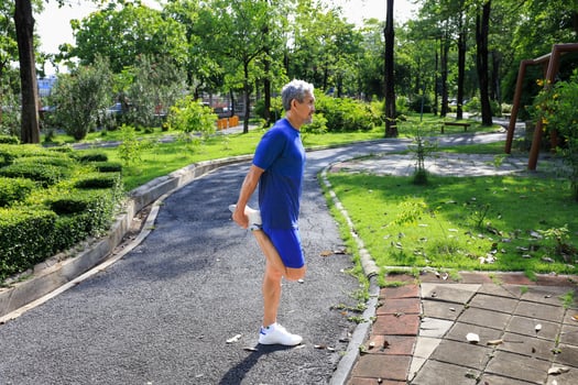 Senior Asian man is stretching his leg muscle during warm up exercise work out in the morning at public park for healthy and longevity concept photo