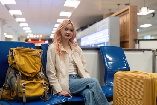 Young Woman Traveling at Airport with Yellow Backpack and Suitcase, Sitting on Blue Chairs in Modern Terminal, Ready for Adventure and Exploration photo
