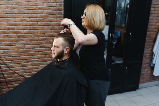 Woman barber cutting hair to a bearded man. photo