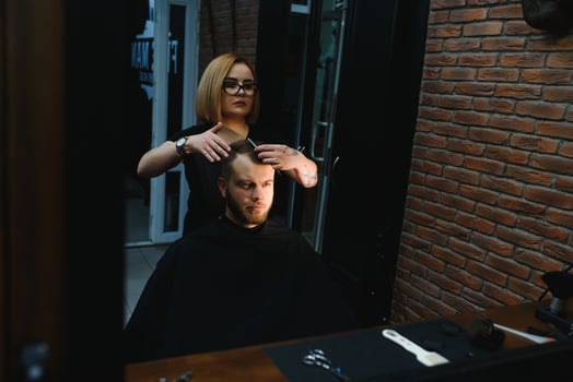 Serving client in Barbershop. Professional barber girl, female hairdresser making modern haircut for a man sitting in barber shop chair. Focus on a girl. Hairdressing, shaving, trimming, grooming photo