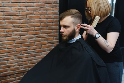 Stylish man sitting barber shop Hairstylist Hairdresser Woman cutting his hair Portrait handsome happy young bearded caucasian guy getting trendy haircut Attractive barber girl working serving client photo