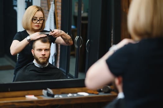 Serving client in Barbershop. Professional barber girl, female hairdresser making modern haircut for a man sitting in barber shop chair. Focus on a girl. Hairdressing, shaving, trimming, grooming photo