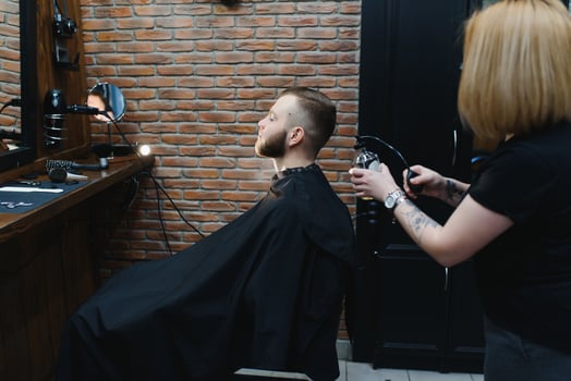 Young adult beautiful caucasian woman hairdresser cuts beard handsome man at modern barbershop Happy gay sitting chair men beauty salon. beard care. metrosexual. Female barber in black gloves serving photo