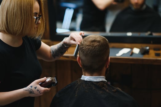 Professional hairdresser woman doing styling of handsome guy with electric hair clipper at barber shop photo