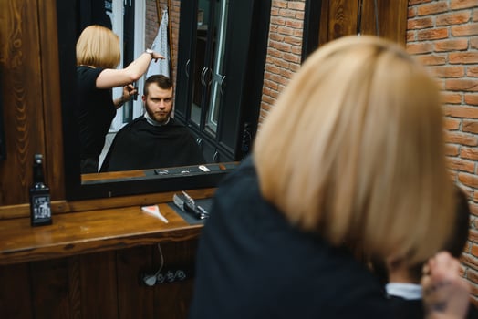 Stylish man sitting barber shop Hairstylist Hairdresser Woman cutting his hair Portrait handsome happy young bearded caucasian guy getting trendy haircut Attractive barber girl working serving client photo