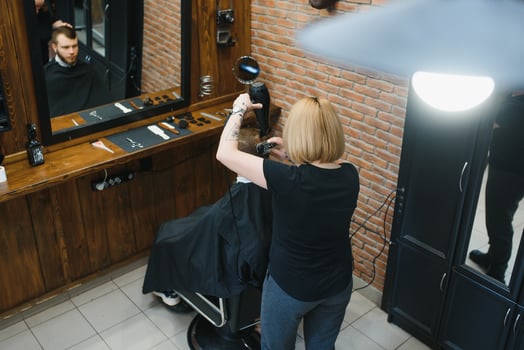 Stylish man sitting barber shop Hairstylist Hairdresser Woman cutting his hair Portrait handsome happy young bearded caucasian guy getting trendy haircut Attractive barber girl working serving client photo