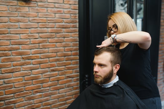 Stylish man sitting barber shop Hairstylist Hairdresser Woman cutting his hair Portrait handsome happy young bearded caucasian guy getting trendy haircut Attractive barber girl working serving client photo
