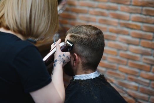 Stylish man sitting barber shop Hairstylist Hairdresser Woman cutting his hair Portrait handsome happy young bearded caucasian guy getting trendy haircut Attractive barber girl working serving client photo