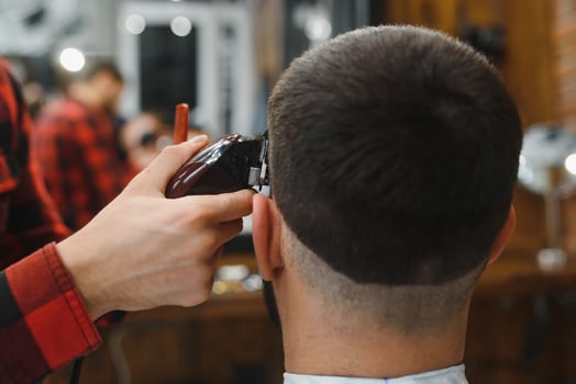 Making haircut look perfect. Young bearded man getting haircut by hairdresser while sitting in chair at barbershop. photo