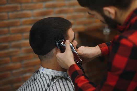 Handsome bearded man is smiling while having his hair cut by hairdresser at the barbershop. photo