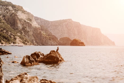 Yoga on the beach. A happy woman meditating in a yoga pose on the beach, surrounded by the ocean and rock mountains, promoting a healthy lifestyle outdoors in nature, and inspiring fitness concept. photo