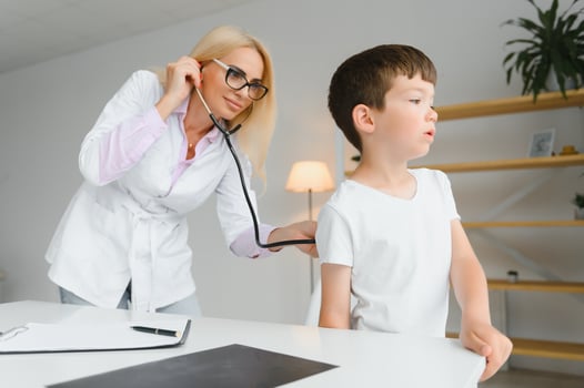 Pediatrician listening to breathing in the lungs and heartbeat with stethoscope. Portrait of adorable little boy visiting doctor. photo