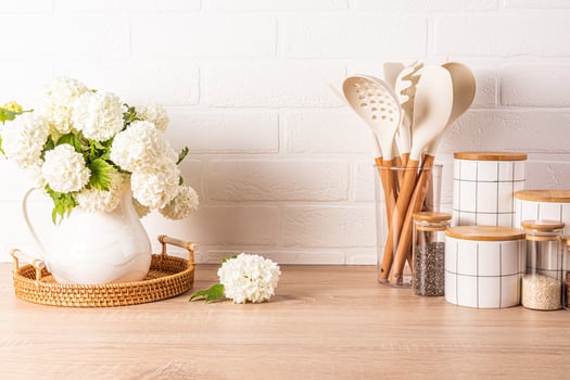 A set of tools for cooking food in a stand, a set of white ceramic jars, a jug with flowering branches in a wooden countertop. Eco style. photo