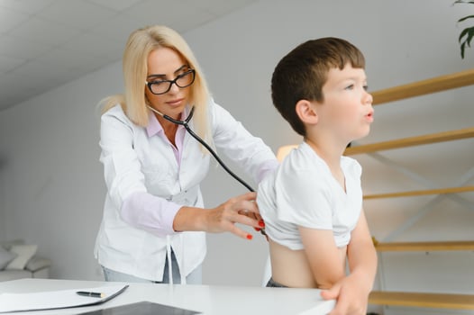 Doctor pediatrician examines child. Female doctor puts a stethoscope to a child's chest and listens to the little boy's heartbeat and lungs. Concept of health care and pediatric medical examination. photo