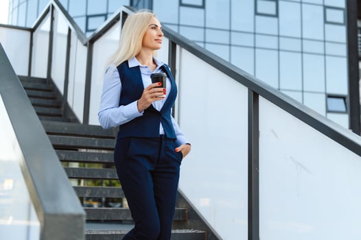 Beautiful Woman Going To Work With Coffee Walking Near Office Building. Portrait Of Successful Business Woman Holding Cup Of Hot Drink. photo