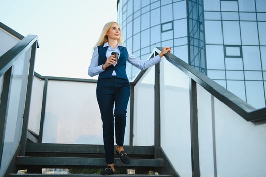 Beautiful Woman Going To Work With Coffee Walking Near Office Building. Portrait Of Successful Business Woman Holding Cup Of Hot Drink. photo