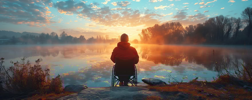 A person in a wheelchair enjoys a peaceful sunrise by the lake, surrounded by nature, reflecting in the water. photo