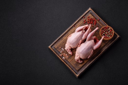 Whole raw quails with salt, spices and herbs on a dark concrete background photo