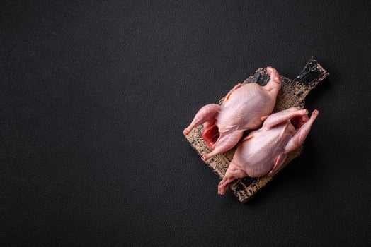 Whole raw quails with salt, spices and herbs on a dark concrete background photo