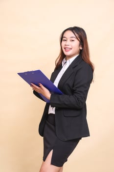 Beautiful formal Asian executive mature woman in suit cheerful smile standing and pose holding clipboard to camera, 3 by 4 body portrait on yellow background for commercial, vacancy and business photo