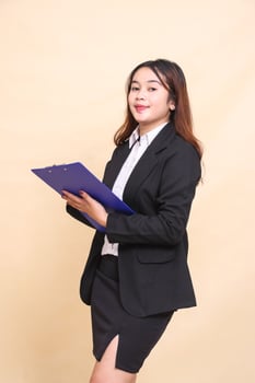Beautiful formal indonesia executive mature girl in suit elegant smile standing and pose holding clipboard to camera, 3 by 4 body portrait on yellow background for commercial, vacancy and business photo