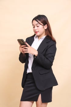 Beautiful formal indonesia executive woman in suit standing candid smile and holding while operating online shopping gadget smartphone on yellow background for commercial, vacancy and business photo