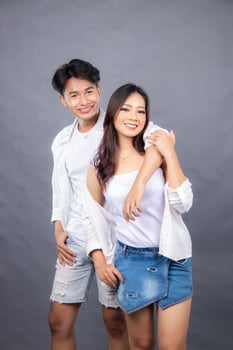 smiling man and woman posing standing in front of camera man's hands embracing woman's body while woman facing sideways indoors. fashion promotion couple photo session in studio