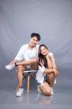 happy smiling man and woman posing sitting in front of the camera while their ladder hugs the woman indoors. fashion promotion couple shirt photo session in gray background studio