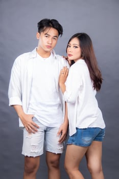 elegant man and woman posing standing in front of camera hand holding arm man while woman facing sideways indoor. fashion promotion couple photo session in studio