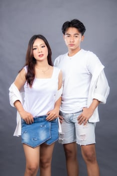 elegant men and women are posing standing in front of the camera with their shirts open, their hands to their waists facing forward in an indoor setting. fashion promotion couple photo session in stud