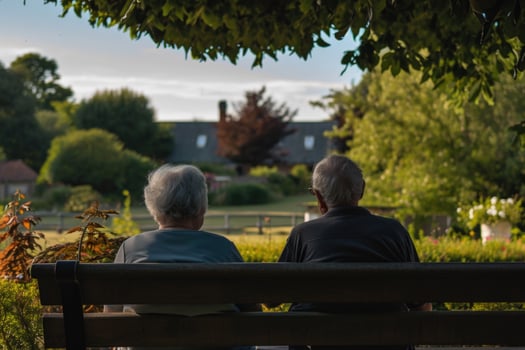 Older couple sitting on a bench in a park looking at a neighborhood photo