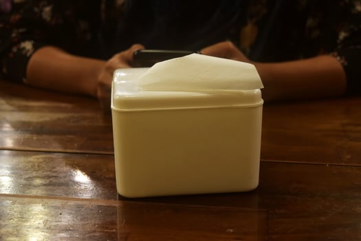 A white tissue holder is on a wooden table photo