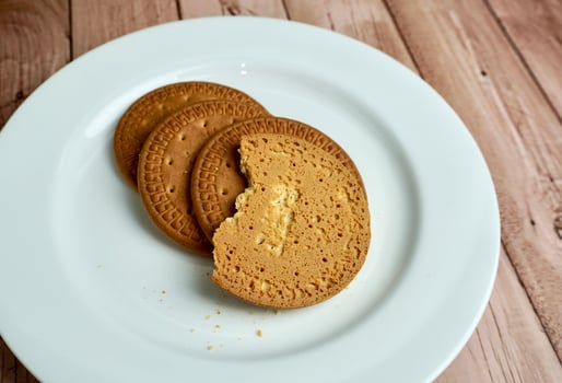 Round brown sweet sugary butter biscuit on top of white plate. Food object photography isolated on wooden surface background. photo