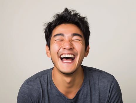 Young Asian Man Laughing Joyfully, Showing Happiness and Positive Emotion, in Casual Gray T-shirt photo