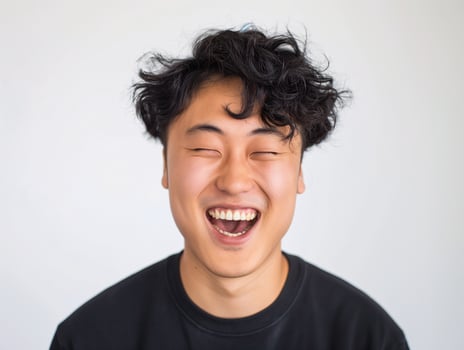 Happy Young Asian Man with Curly Hair Laughing, Displaying Positive Emotion in Casual Black Shirt photo