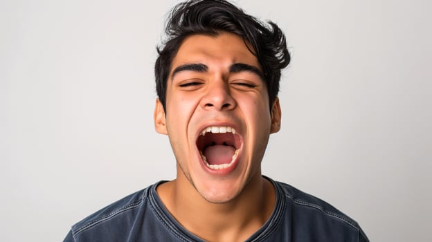 Close-up Portrait of a Young Man Yawning Widely, Expressing Exhaustion and Sleepiness Indoors photo