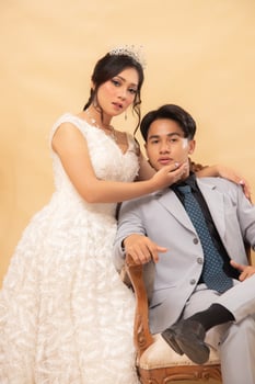 elegant male and female couple poses standing relaxed smiling slightly looking forward girl's hands hold cheeks on arm of chair affectionately indoor photo shot. couple wedding national bride studio