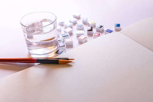 Watercolor paints, brushes, water in glass and paper on white background. Flat lay, top view photo