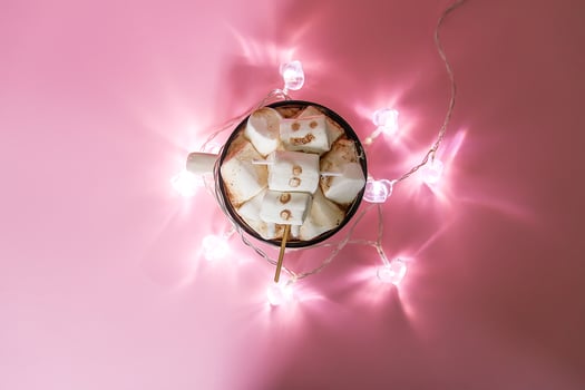 Hot fresh cocoa drink in ceramic cup with marshmallow and glass garland on soft pink background. photo