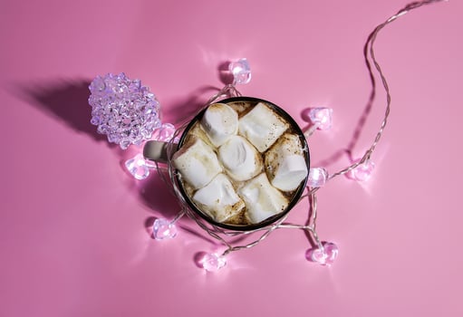 Ceramic mug with hot fresh cocoa drink with marshmalllow and garland with glass fir-tree on soft pink background. photo