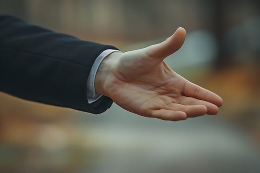 A person in a suit extends their hand for a handshake photo
