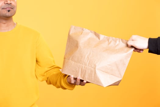 Catering food delivery service employee giving order to client. Close up shot of delivery worker offering lunch paper bag to hungry customer, isolated over studio background photo