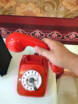 A person picks up a red telephone receiver to make or receive a telephone call with someone. Red rotary telephone with cable. photo